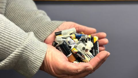 A person's hands cupping a pile of recycled batteries