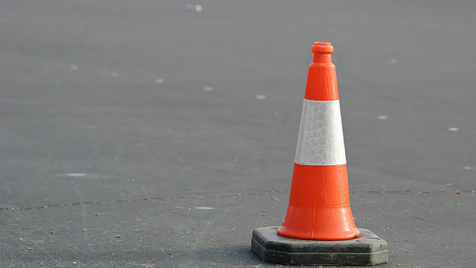 A traffic cone on a bitumen road surface banner image