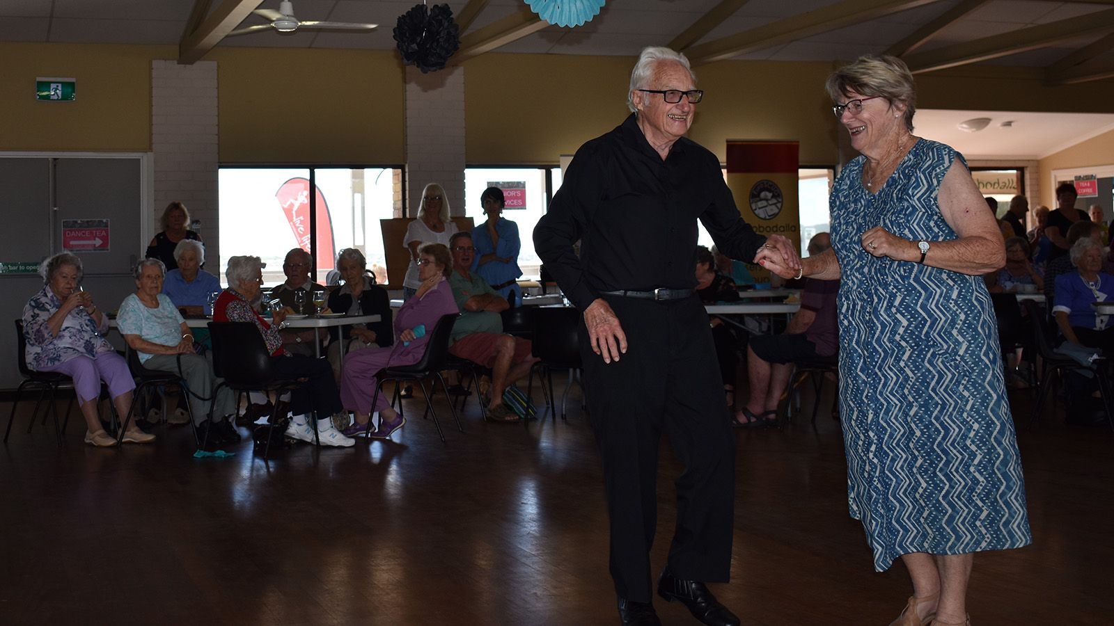 An older man and woman dancing at a social event banner image