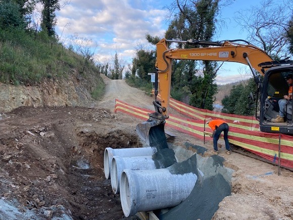 Image An excavator places gravel around concrete culverts that go beneath a dirt road.