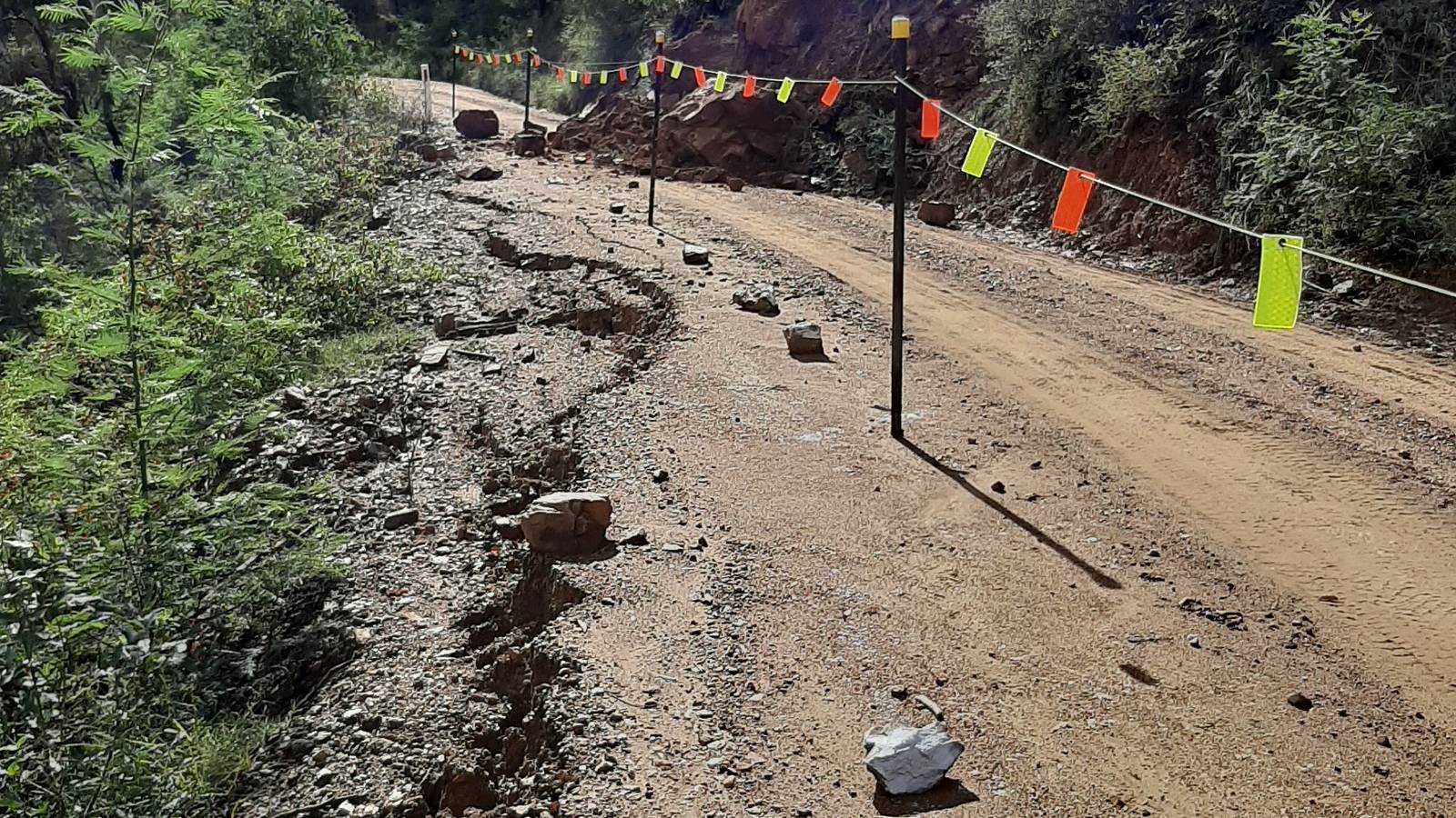 Extensive cracks are visible on the low side of a dirt road with a landslide visible in the background