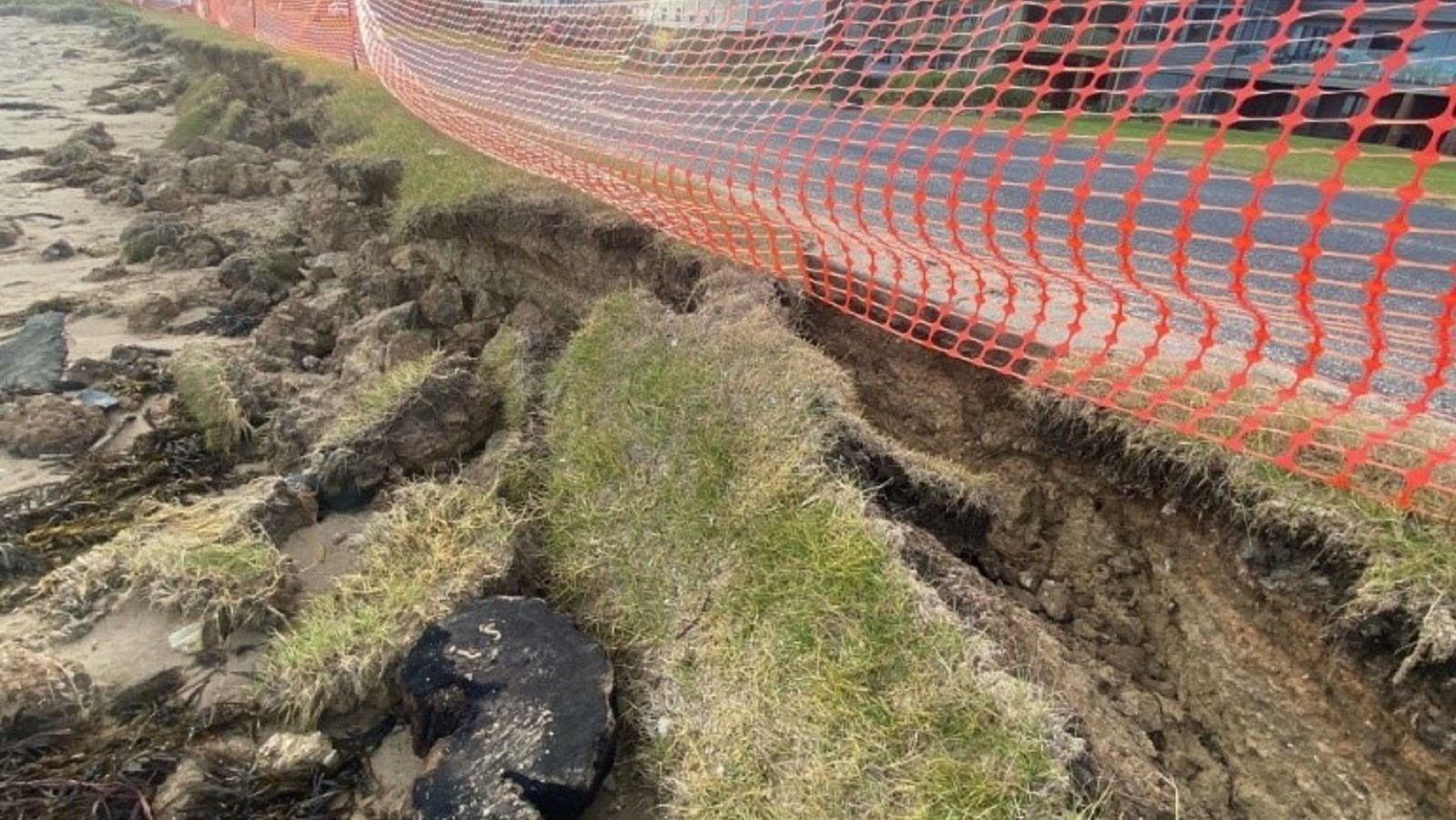 Image Chunks of grassed earth have collapsed onto a beach next to a sealed road.