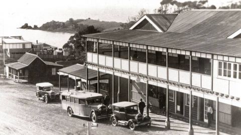 A black and white photo of Lynch's Hotel, Narooma showing vintage cars and a view down the hill to the water.