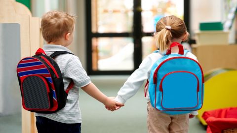 Two children wearing backpacks and holding hands.