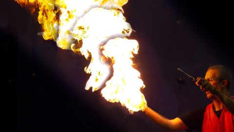 Man blowing through a pipe with a fire at the end
