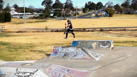 Guy doing a trick at a skatepark with suburban background