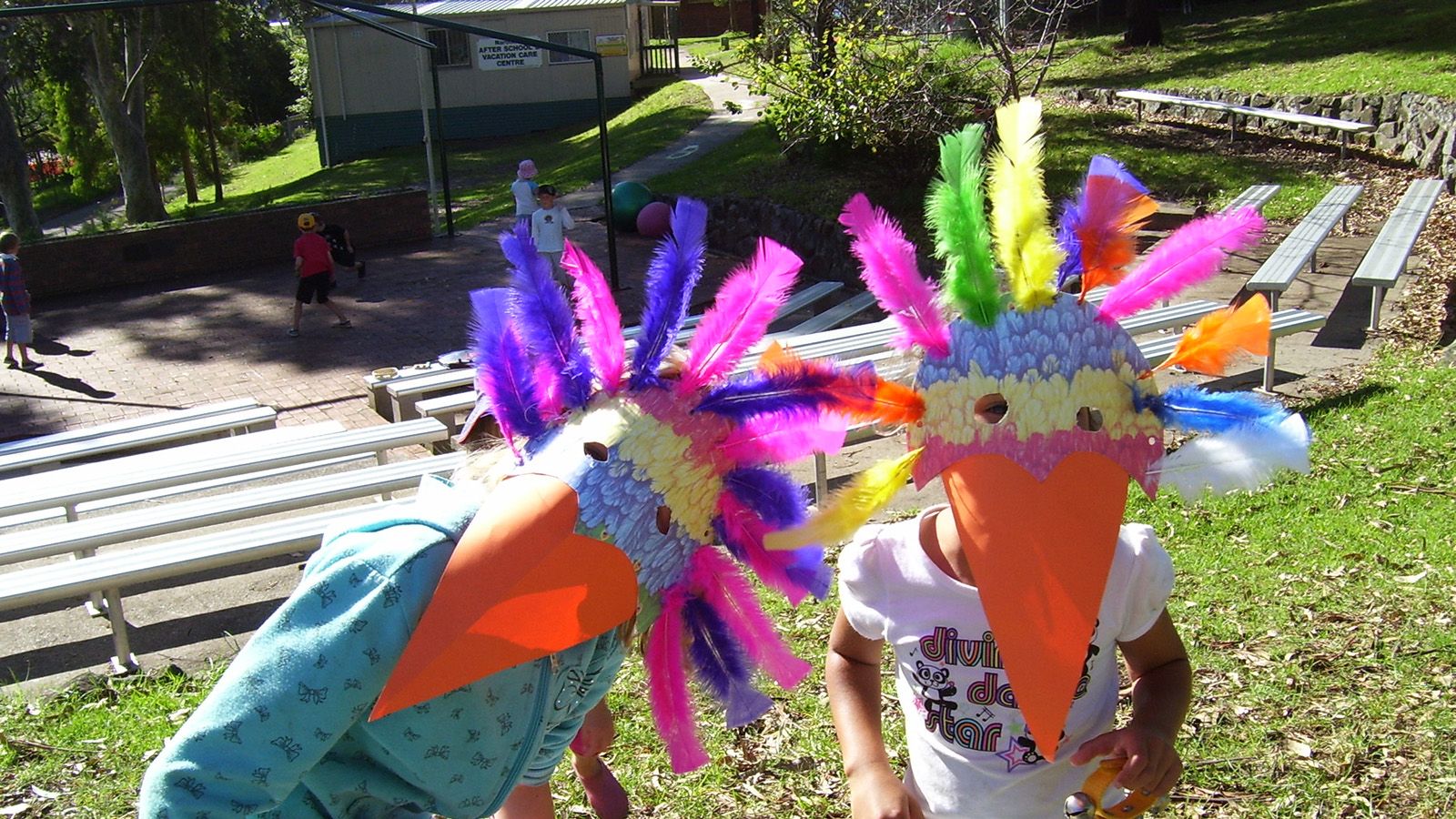 Two children wearing colourful home made bird masks over their faces banner image