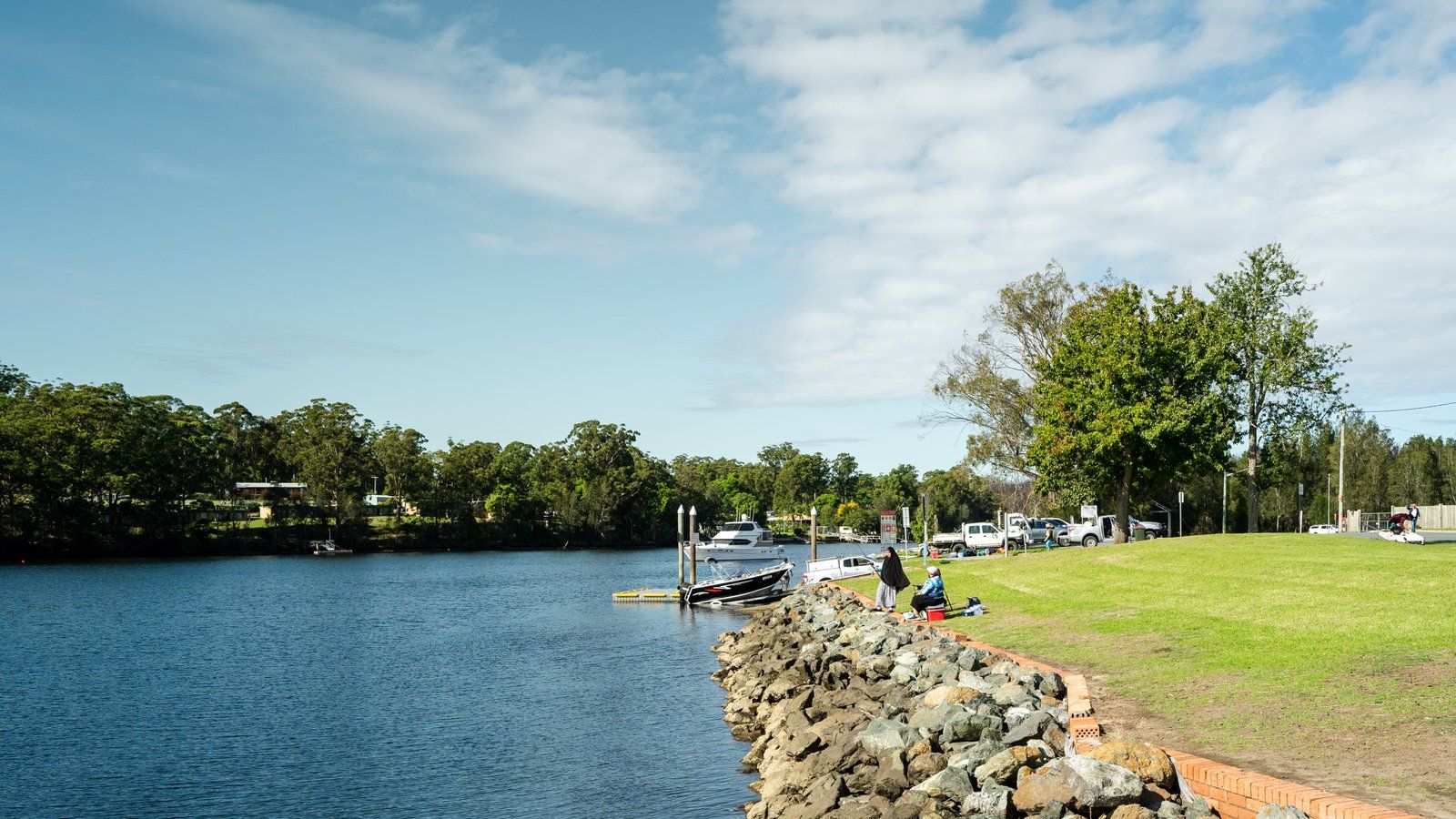 People fishing along the waterfront with grassy area behind them banner image