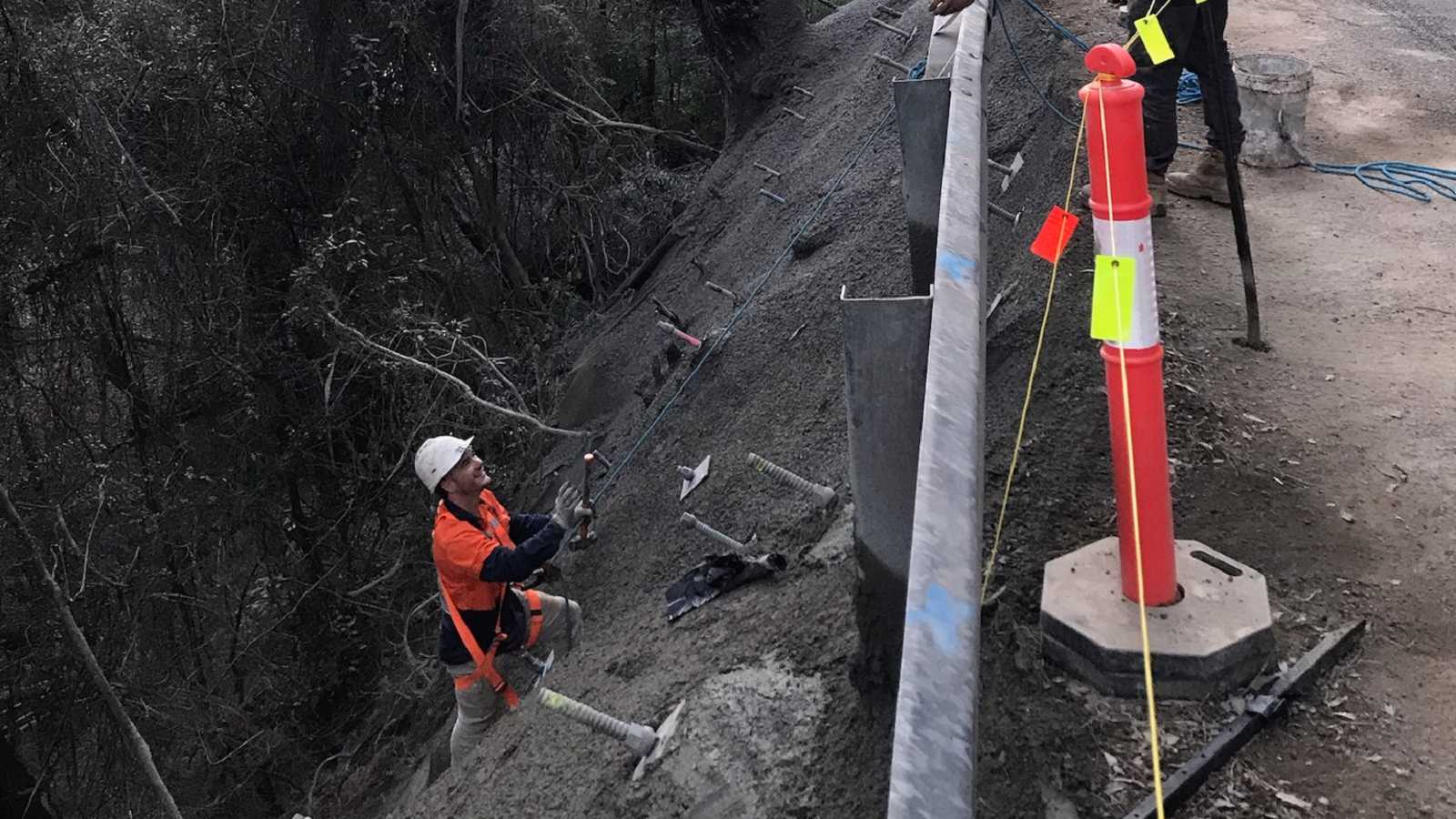 A man works on a steep slope to secure the roadside.