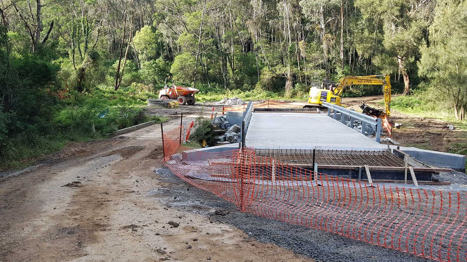 A concrete bridge is under constructin next to a smaller, timber bridge.