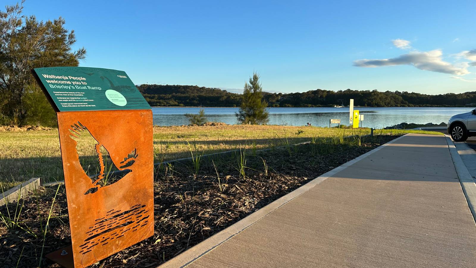 Image An interpretive sign is next to a pathway leading to a water body.