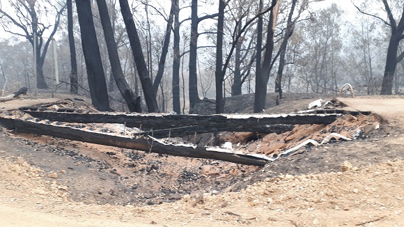 Image Two burnt timber bridge girders straddle a dry creek bed