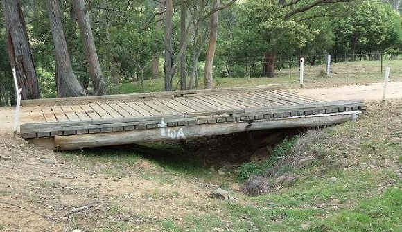 Image A single span timber bridge crosses a small gully