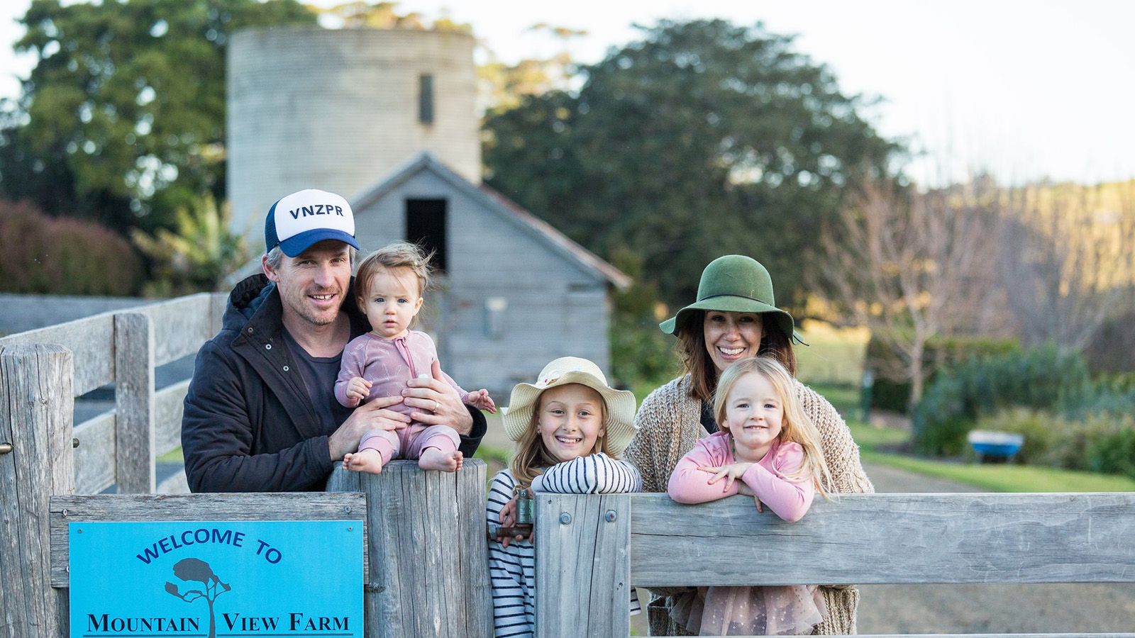 A young family of five standing behind a farm style fence banner image