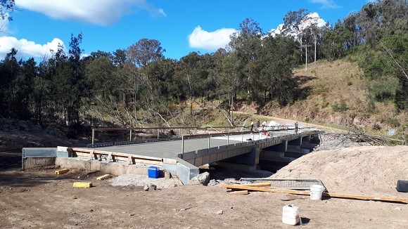 Image People work on a concrete bridge under construction in a rural setting.