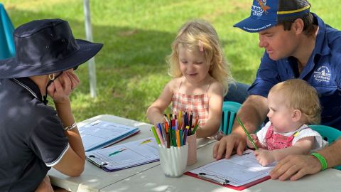 Female council staff member watches as two children colouring in with father.