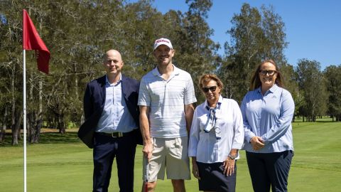 group of four people standing on a golf course near red putting flag