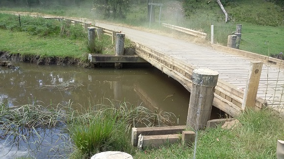 Image A low single span timber bridge crosses over a creek.