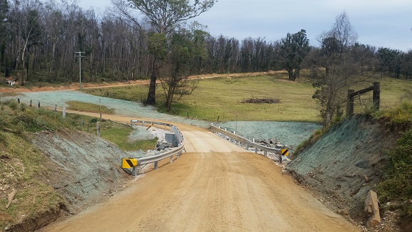 Image Guardrail aligns a new bridge on a dirt road.