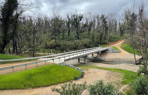 Image A concrete bridge on a dirt road passes over a gravelly creek.