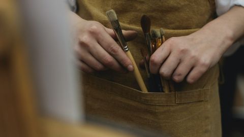 A close up shot of an artist's apron with paintbrushes in the pocket.