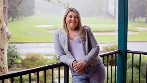 A smiling woman leaning against the railing with a golf course in the background.