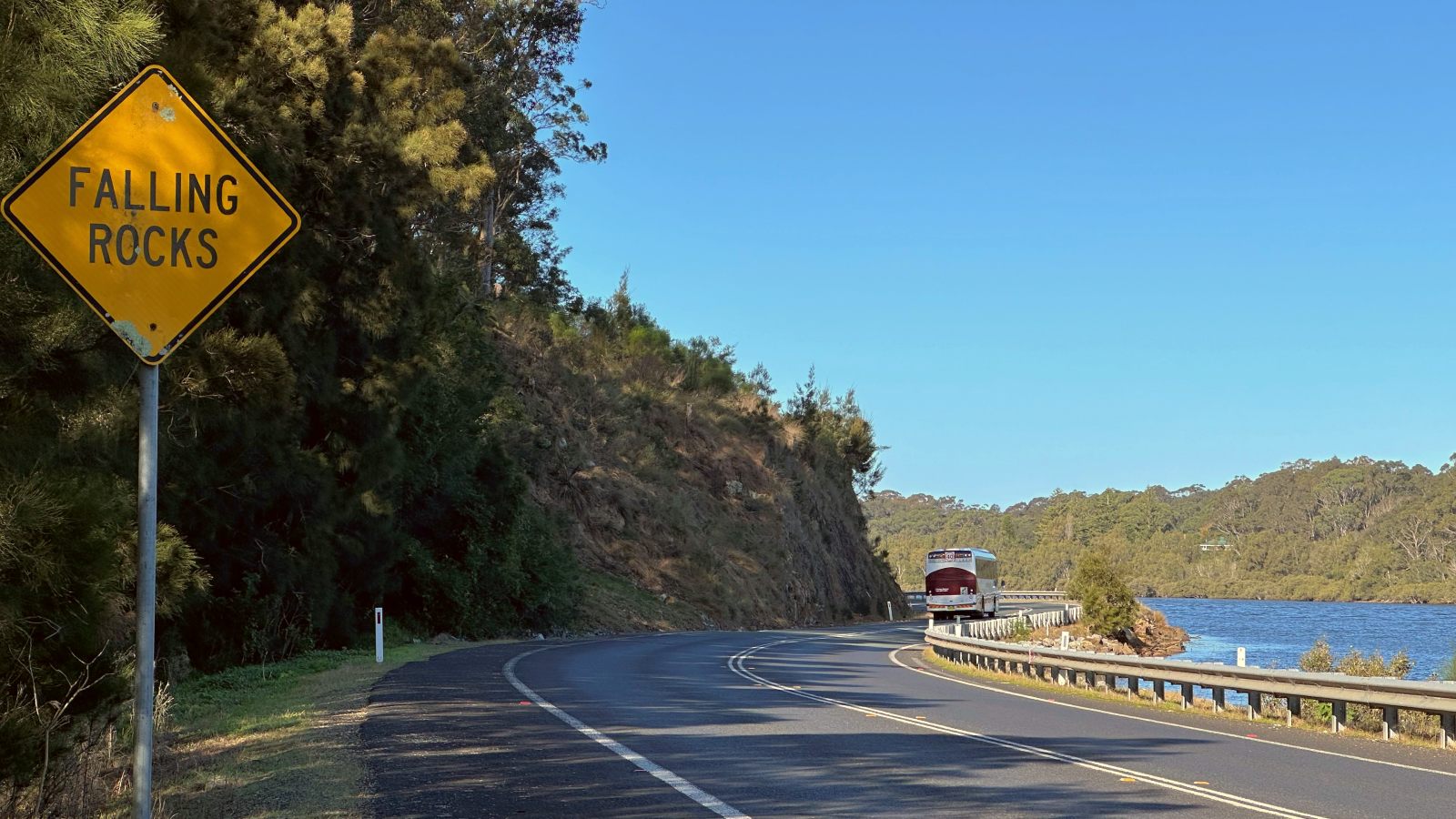 Image A falling rocks sign warns commuters along a winding road between a cliff and a body of water