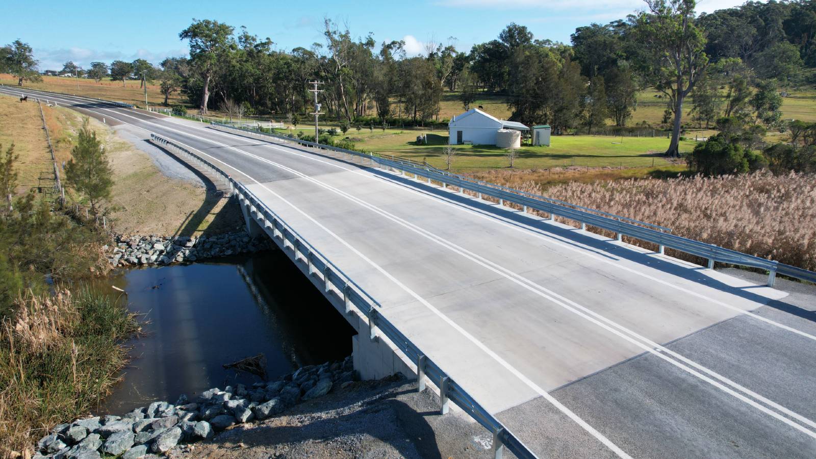Image A concrete bridge lined with guardrail crosses a creek in farmland