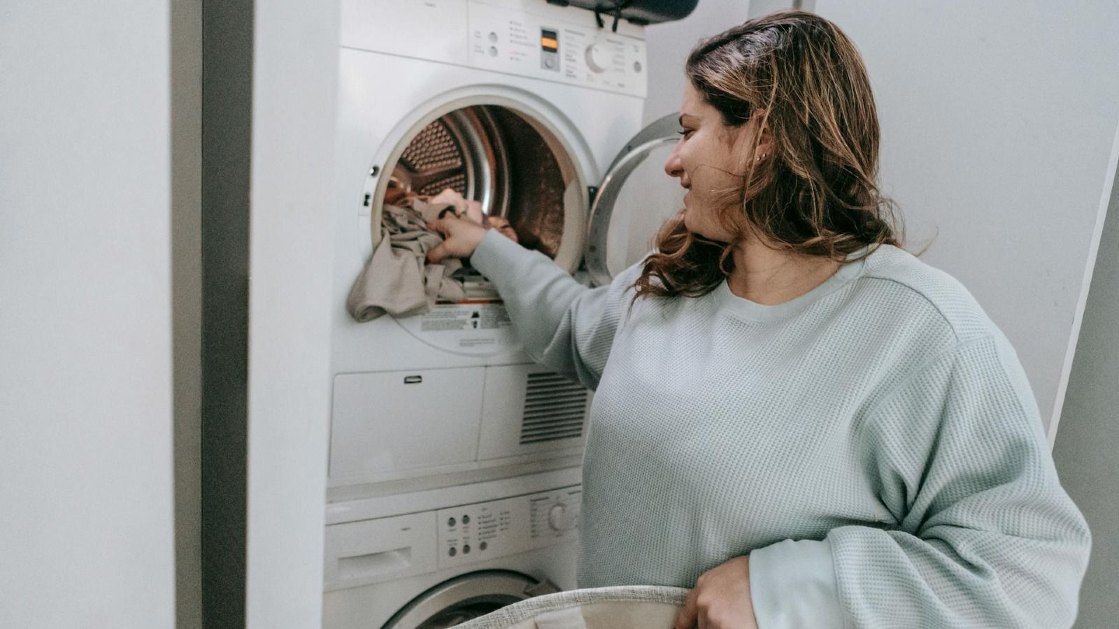 A woman kneeling down and reaching into a clothes washing machine banner image