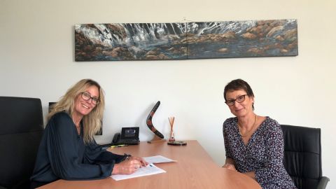 Two ladies sit either side of a desk.