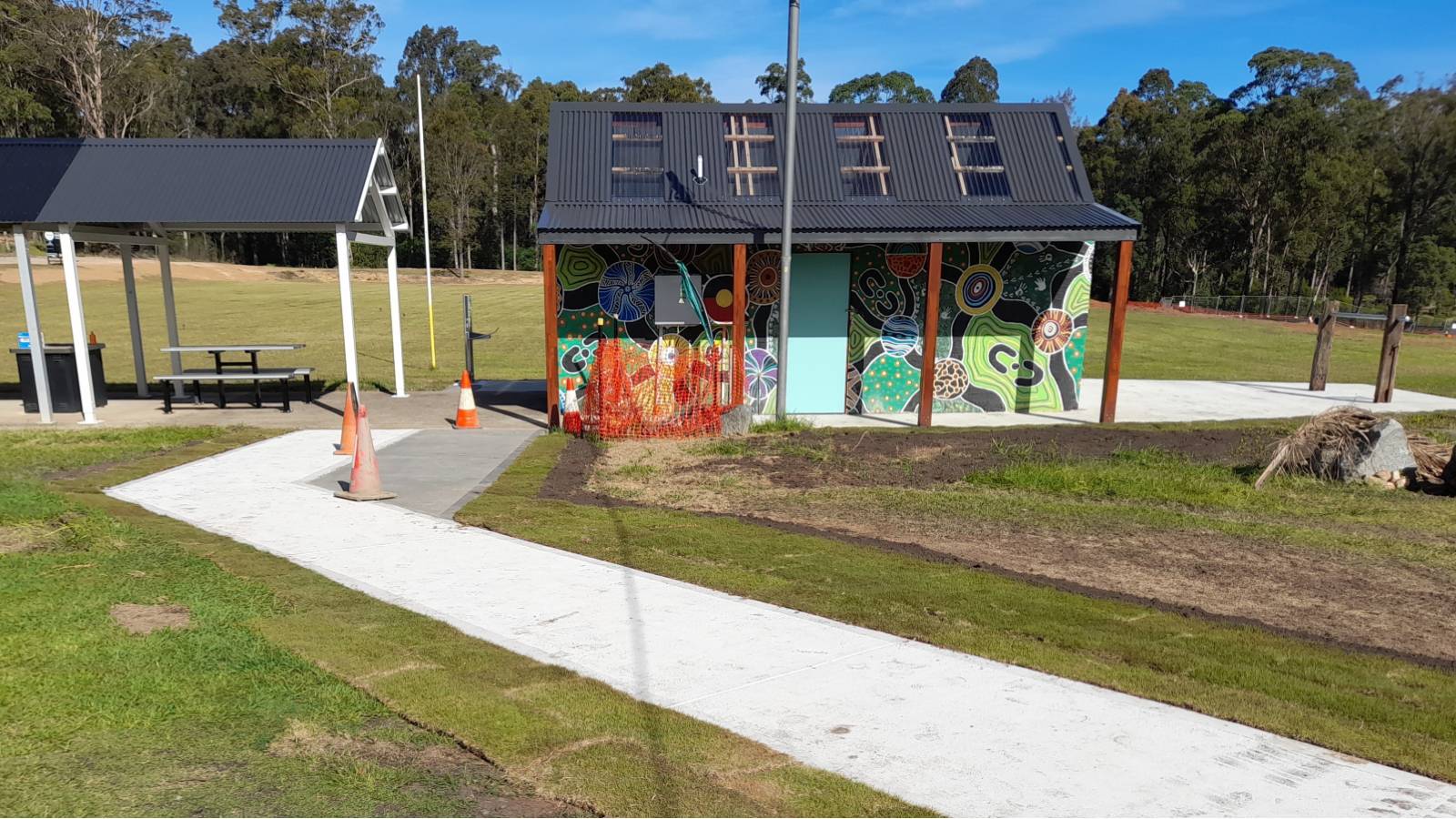 Image A public toilet block decorated with Aboriginal artwork, with a covered bbq seating on one side and a mountain bike wash area to the other.