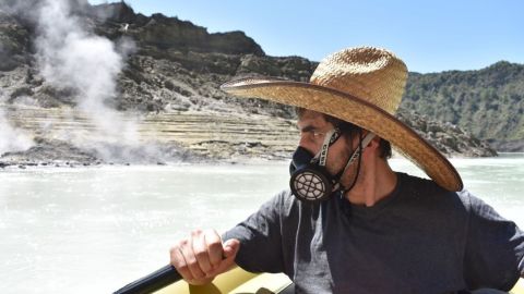 A man in a small boat, wearing a gas mask, on a toxic lake.