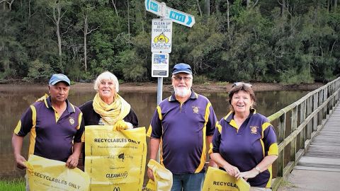 Two men and two women holding yellow garbage bags in front of inlet