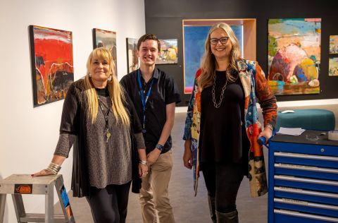 Two woman either side of a man in an art gallery