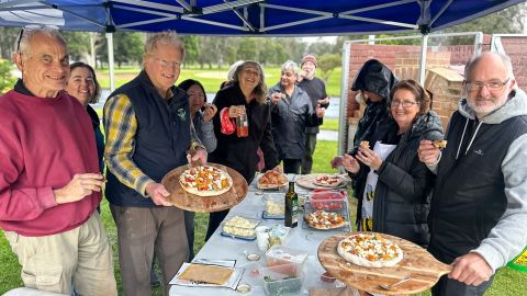 a group of people standing around a table with pizzas