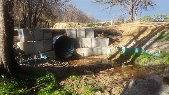 Image A steel pipe runs under the road supported by large concrete blocks