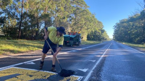 A Council worker fills a pothole with black gravel using a shovel.