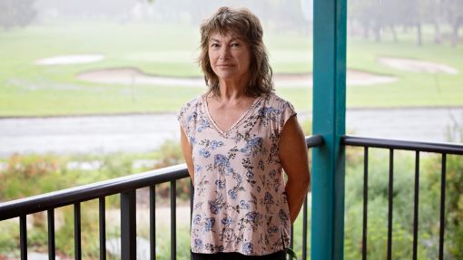 Dark haired woman standing next to a verandah railing with the golf course in the background.
