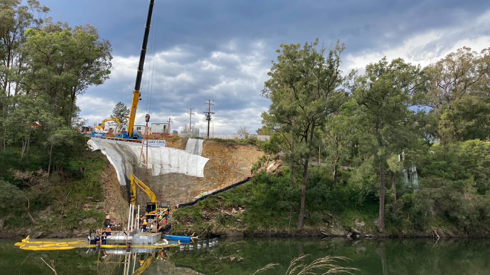 A large crane lowers a pipe into the water below a large excavated site/