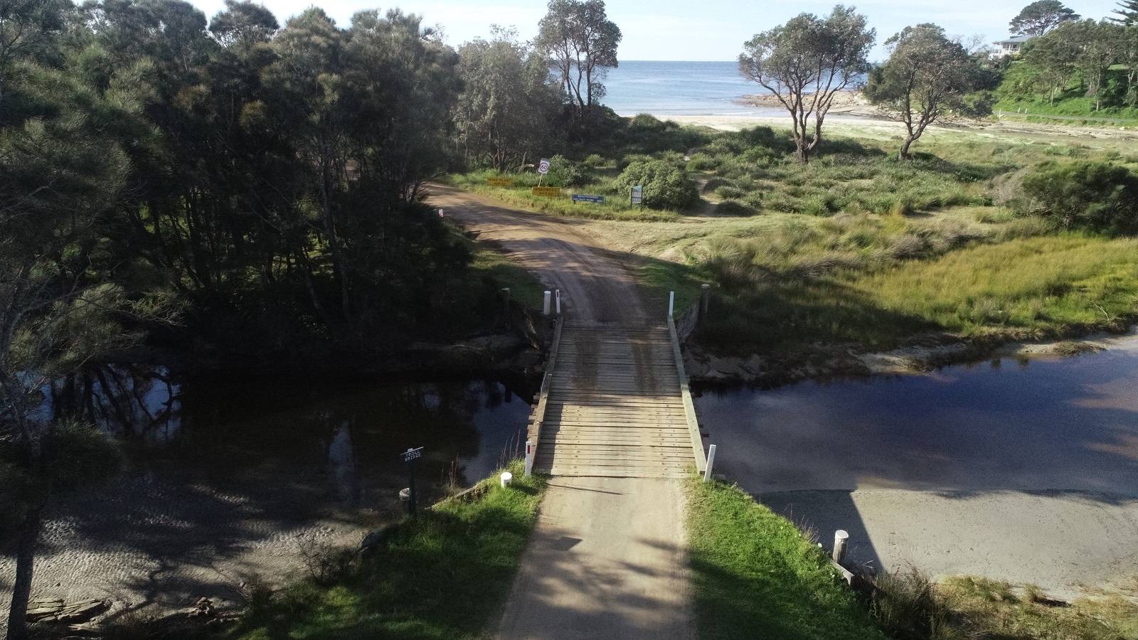 A short timber bridge leads over a coastal creek