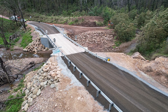 Image An aerial view of a new concrete bridge lined with guardrail crosses over a creek in bushland.