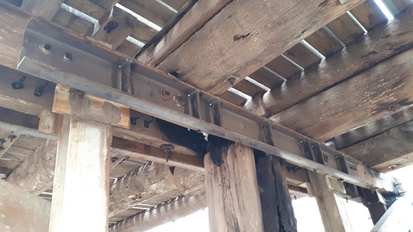 Image A large steel beam is bolted to the underside of a timber bridge