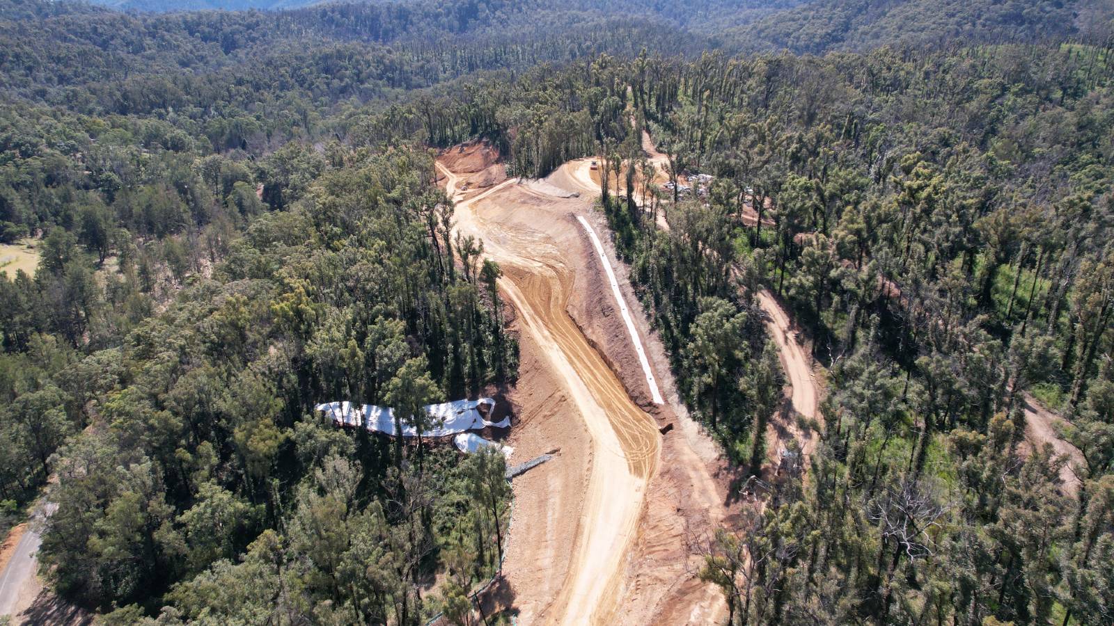 An aerial photo shows a dirt road under construction leading through a forest