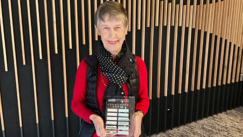 A lady stands holding glass award that says 