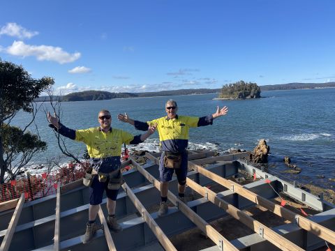 Man kneeling, building a deck overlooking water 