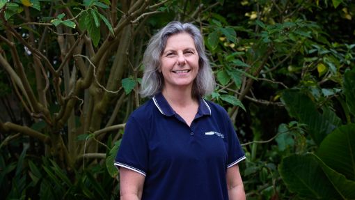 Smiling woman in blue shirt standing in front of background of vegetation.