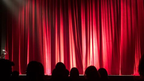 Image of a stage with a large red curtain pulled closed covering the stage.
