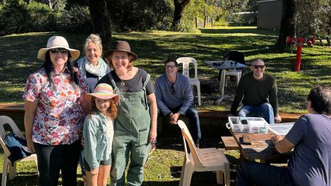 a family standing and smiling with other people sitting down behind them.