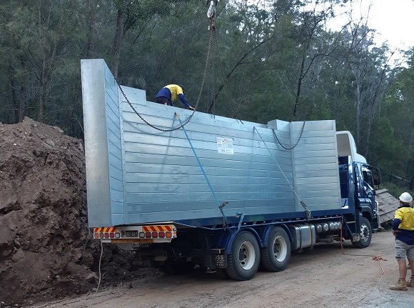 Image A large refabricated bridge abutment is prepped for unloading off a delivery truck