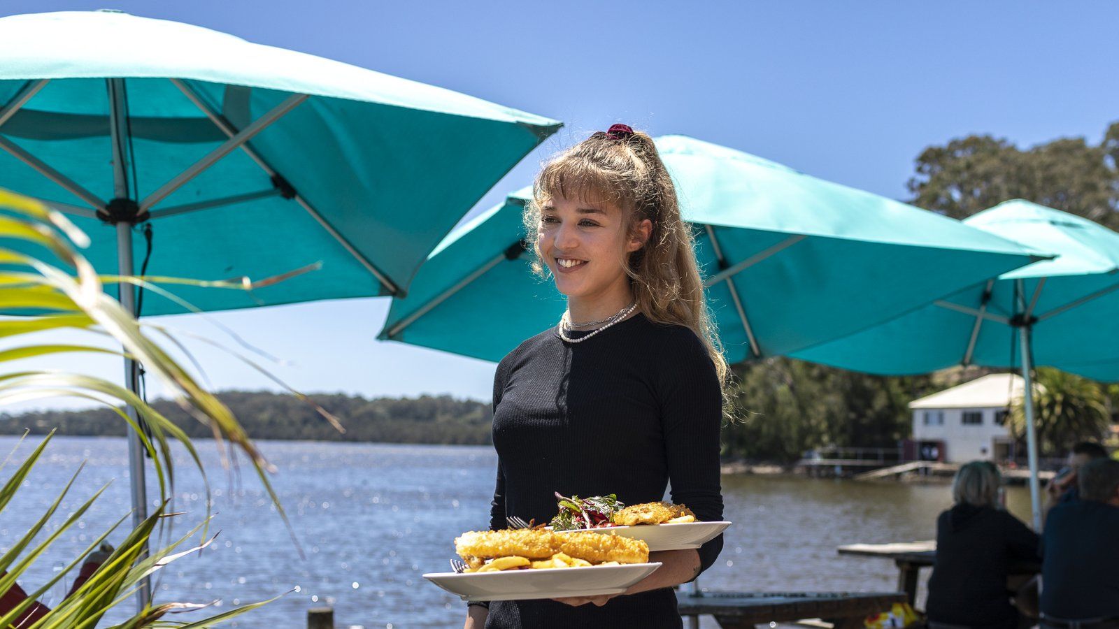 Woman holding plates of fish and chips in one arm by the water banner image